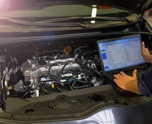 Auto electrician running a laptop diagnostic on a car engine